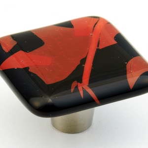 May include: Square glass cabinet knob with a black and red abstract design. The knob has a brushed nickel base.