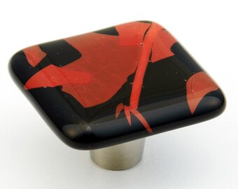 May include: Square glass cabinet knob with a black and red abstract design. The knob has a brushed nickel base.