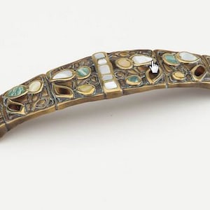 May include: A brass door handle with a decorative design featuring inlaid green, white, and brown stones.