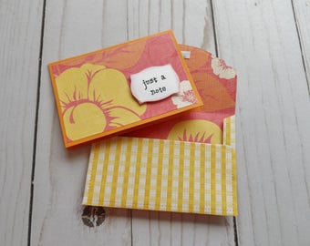 May include: A yellow and orange floral card with a white envelope. The card has the text "just a note" on it.