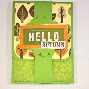 May include: A handmade autumn-themed greeting card. The card features a green and yellow color scheme with a tree pattern. The words "HELLO AUTUMN" are displayed on the front of the card.