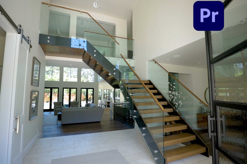 Op de afbeelding: Een modern huisinterieur met een glazen en houten trap die naar de tweede verdieping leidt. De trap heeft een glazen leuning en een houten handrail. Het huis heeft grote ramen en een wit interieur.