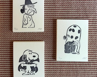Puede incluir: Tres tarjetas rectangulares blancas con ilustraciones en tinta negra. Una muestra una bruja con sombrero puntiagudo, otra un perro disfrazado de vampiro y la tercera una figura fantasmal con puntos sosteniendo una caja. Cada tarjeta tiene 1/20 y ABP.