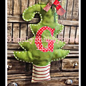 May include: A green burlap Christmas tree door hanger with white polka dots and a red and white striped base. The tree has a red felt letter "C" with white polka dots in the center. The text "Simply Shabby by Dee" is visible in the background.