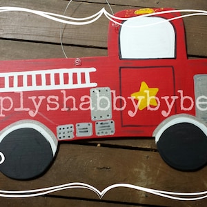May include: Red wooden fire truck door hanger with white ladder details, a yellow star, and black wheels.  The truck has a white painted area for personalization.