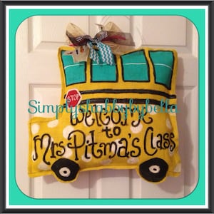 May include: A yellow school bus door hanger with white polka dots, a stop sign, and the text "Welcome to Mrs. Pitma's Class".