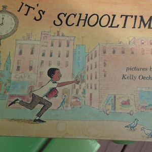 May include: A vintage children's book cover with the title "It's Schooltime" in large, bold letters. The cover features a colorful illustration of a young boy running towards a school building in a city setting. The illustration is in a cartoon style and includes a clock tower, buildings, and a street scene. The text "pictures by Kelly Oechsli" is printed in the bottom right corner.