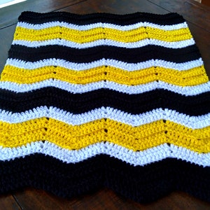 May include: A crocheted blanket with a chevron pattern in black, white, and yellow.