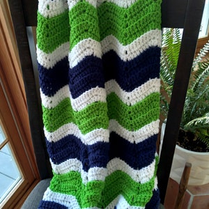 May include: A crocheted blanket with a chevron pattern in green, white, and navy blue.