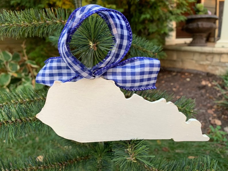 May include: White wooden ornament shaped like the state of Kentucky, decorated with a blue and white gingham ribbon.