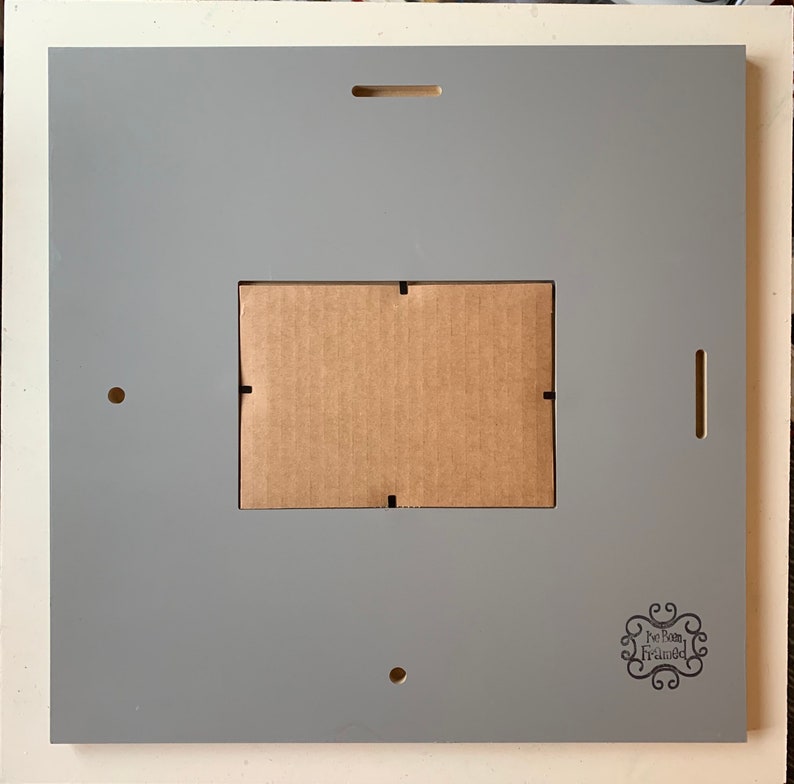 May include: A gray picture frame with a brown cardboard insert. The frame has a small logo that says "We Both Framed" in a decorative font.