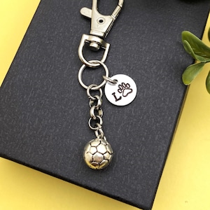 May include: Silver keychain with a soccer ball charm and a personalized tag with the letter "L" and a paw print.
