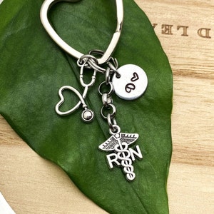 May include: Silver heart-shaped keychain with a stethoscope, a small heart charm, a charm with the letter "D" and a heart, and a charm with the medical symbol and the letters "RN".