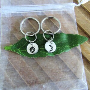 May include: Two silver keychains with a sun and moon design. The keychains are on a green leaf and a white background.