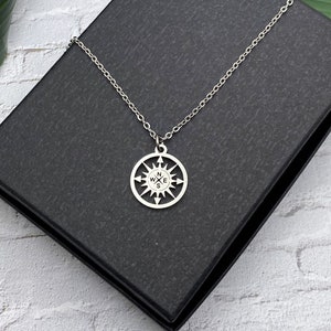 May include: A silver necklace with a compass pendant. The compass has the letters N, W, E, and S inscribed on it.