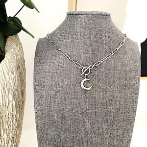 May include: A silver chain necklace with a crescent moon pendant. The chain has a toggle clasp.