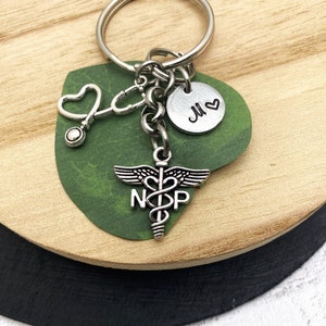 May include: Silver keychain with a stethoscope, a heart charm, a medical caduceus charm with the letters "NP" and a round charm with the letter "M" and a heart.