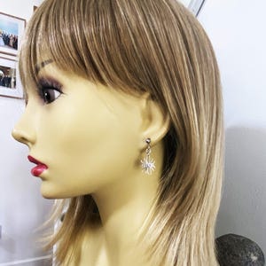 May include: A pair of silver dangle earrings featuring a small bee design. The earrings are worn by a model with blonde hair.