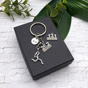 May include: A silver keychain with a running figure charm, a heart charm with the letter "K" on it, and two charms with the text "13.1 Marathon" and "26.2 Marathon".