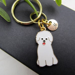 May include: Gold keychain with a white Bichon Frise charm and a gold charm with the letter M.