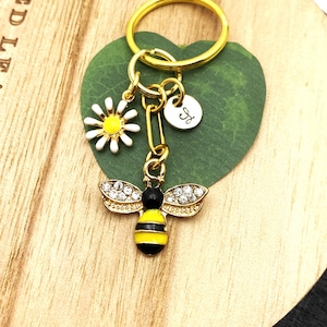 May include: Gold key chain with a bee charm, a daisy charm, and a round charm with the letter "J" on it.