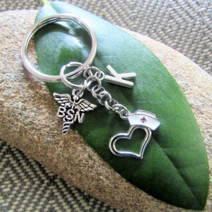 May include: Silver keychain with a heart, a nurse's cap, a medical symbol with the letters BSN, and a letter K charm.