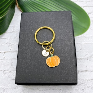 May include: Gold keychain with a small pumpkin charm and a letter 'G' charm. The keychain is in a black gift box.