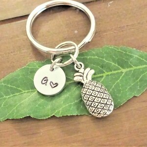 May include: Silver pineapple keychain with a silver charm that has the letter G and a heart on it.