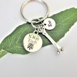 May include: Silver keychain with a bone charm, a round charm with the text "X-Ray Tech" and a small heart charm with the letter "K".