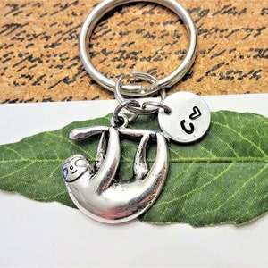 May include: Silver sloth keychain with a small silver charm that says "C ♥". The keychain is hanging from a silver key ring.