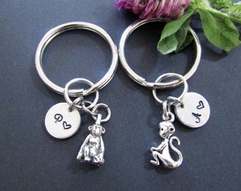 May include: Two silver keyrings with monkey charms and engraved silver discs. The discs say "A" and "Q" with a heart symbol next to each letter.