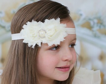 May include: A young girl with long brown hair is wearing a white headband with a white flower embellishment and a pearl-like center. The headband is made of a soft, stretchy material and is perfect for adding a touch of elegance to any outfit.