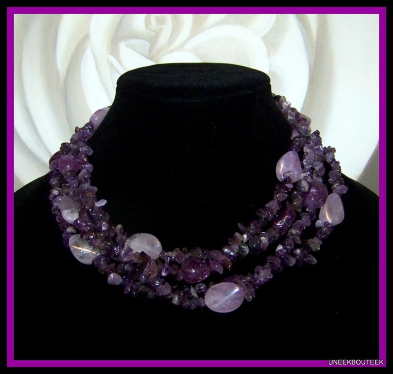 May include: A multi-strand necklace made of amethyst gemstones. The necklace is made of small, irregular shaped stones and larger, oval-shaped stones. The necklace is a deep purple color.