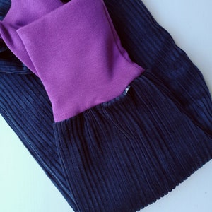 May include: A pair of dark blue corduroy pants with a purple waistband. The pants are folded in half and the waistband is visible.