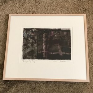 May include: Abstract artwork titled "Burgundy Heap" in a light wood frame. The artwork features dark, textured brushstrokes in shades of black, gray, and burgundy. Signed "Mindy Weisel 1999" in the lower right corner.