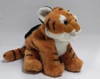 Pode incluir: Um brinquedo de pelúcia de um filhote de tigre com listras laranja e pretas, detalhes brancos no rosto e no peito e pelo preto na parte de trás da cabeça.