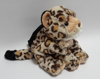 May include: A plush leopard toy with a black backpack. The leopard has a tan and brown spotted pattern, with a white muzzle and black eyes. The toy is sitting on a white surface.