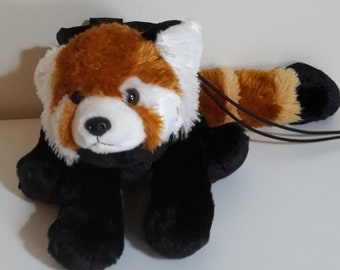 Pode incluir: Um brinquedo de pelúcia de panda vermelho com pelo preto e branco. O brinquedo tem uma cauda longa e uma alça preta.