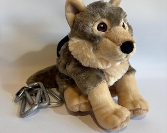 May include: A plush gray and brown wolf with black eyes and a black nose. The wolf is sitting with its legs tucked under its body. There are five silver metal carabiners next to the wolf.