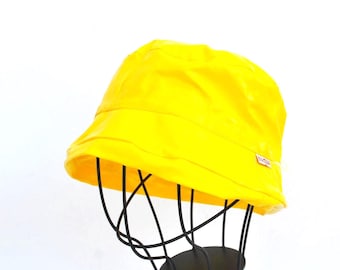 May include: A bright yellow bucket hat with a shiny finish. The hat is on a black display stand.