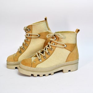 Peut inclure: Une paire de bottes de randonnée en toile beige et daim avec des lacets. Les bottes ont une semelle épaisse blanche.