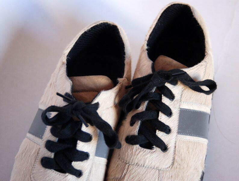 May include: A pair of white leather trainers with black laces and a grey stripe on each side. The shoes have a furry texture.