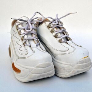 Puede incluir: Un par de zapatillas blancas de plataforma con cordones blancos. Las zapatillas tienen una suela gruesa y robusta y est&aacute;n ligeramente desgastadas.