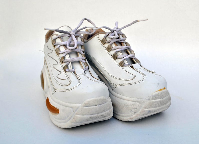 Puede incluir: Un par de zapatillas blancas de plataforma con cordones blancos. Las zapatillas tienen una suela gruesa y robusta y est&aacute;n ligeramente desgastadas.