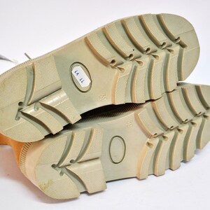 May include: Close-up of the soles of a pair of tan suede boots with a light brown rubber outsole. The boots are size 39 and have a label that reads "KA 11".