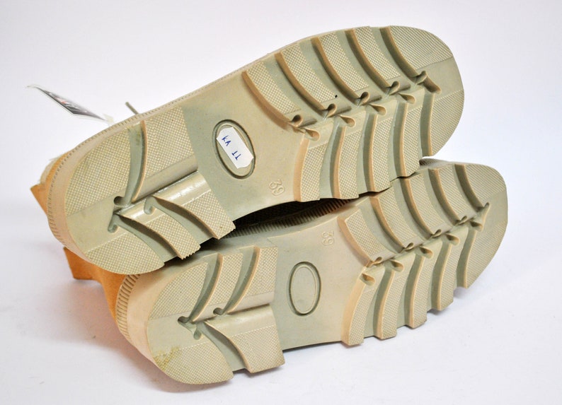 May include: Close-up of the soles of a pair of tan suede boots with a light brown rubber outsole. The boots are size 39 and have a label that reads "KA 11".