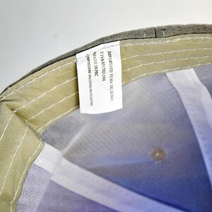 May include: A gray baseball cap with a white mesh lining. The tag on the inside of the cap reads "Importato Verna, Srl Roma, P.IVA 05117611006, Made in PRC, composizione: 100% poliestere."