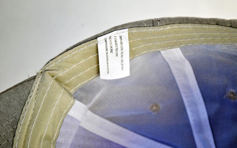 May include: A gray baseball cap with a white mesh lining. The tag on the inside of the cap reads "Importato Verna, Srl Roma, P.IVA 05117611006, Made in PRC, composizione: 100% poliestere."