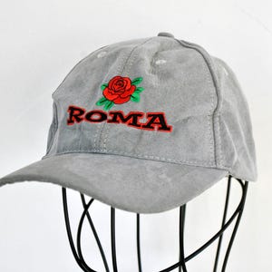 May include: A gray suede baseball cap with a red rose and the word "ROMA" embroidered on the front.