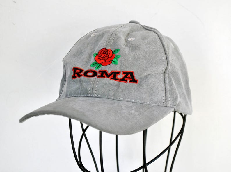 May include: A gray suede baseball cap with a red rose and the word "ROMA" embroidered on the front.